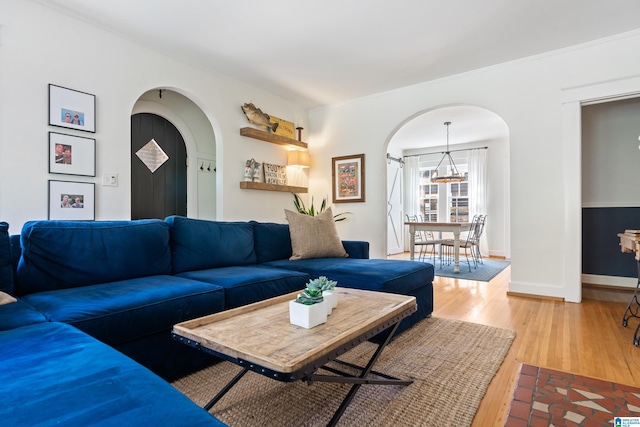 living area featuring arched walkways, light wood finished floors, baseboards, a chandelier, and crown molding