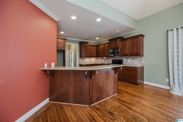 kitchen featuring stainless steel microwave, baseboards, a breakfast bar area, crown molding, and dark wood-type flooring