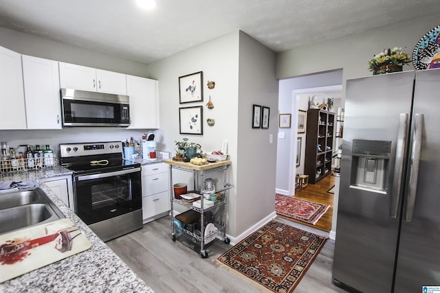 kitchen with stainless steel appliances, light wood-style floors, white cabinetry, and a sink