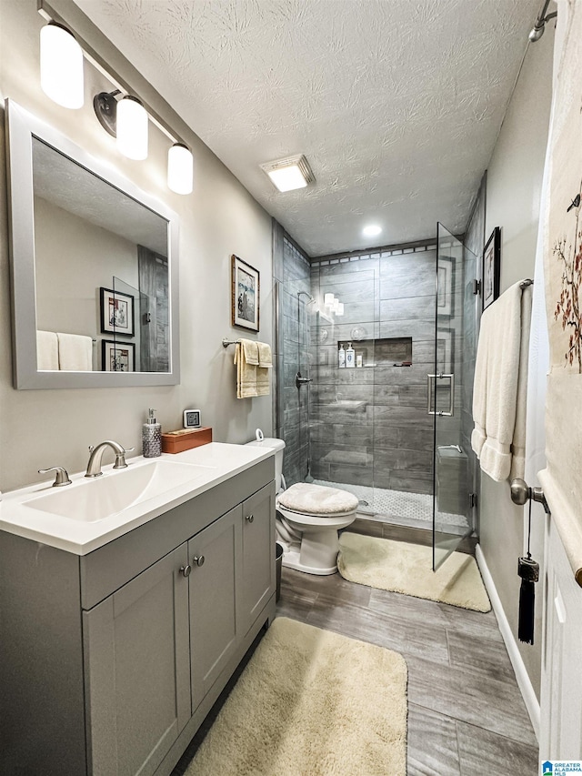 full bathroom with wood finished floors, a stall shower, a textured ceiling, toilet, and vanity