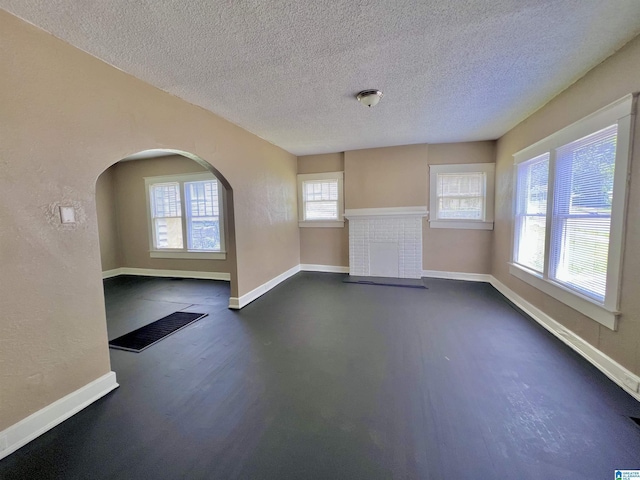 unfurnished living room with baseboards, healthy amount of natural light, a textured ceiling, and a fireplace