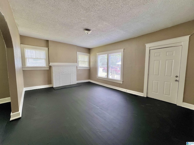 unfurnished living room featuring baseboards, dark wood-type flooring, a textured ceiling, a fireplace, and arched walkways