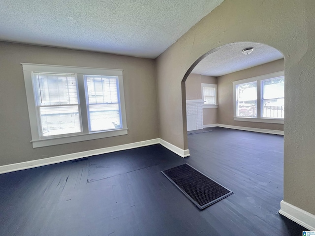 unfurnished room with arched walkways, a textured ceiling, dark wood-style floors, and baseboards