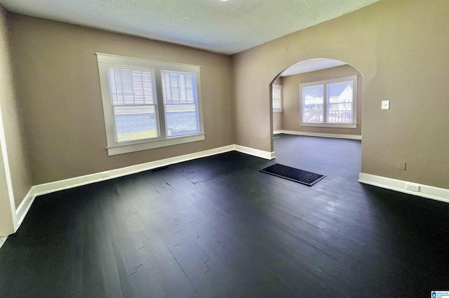spare room with arched walkways, dark wood-style floors, baseboards, and a textured ceiling