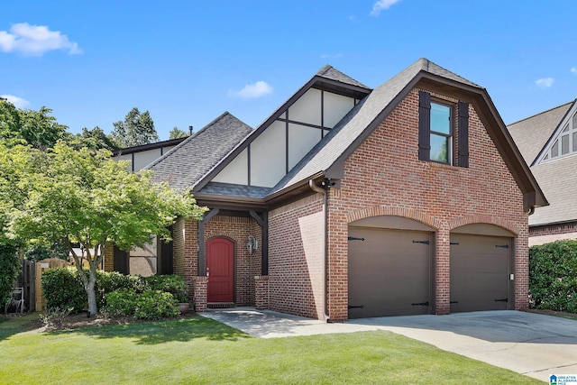tudor home with brick siding, roof with shingles, a garage, concrete driveway, and a front lawn
