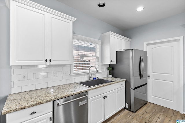 kitchen with stainless steel appliances, a sink, light wood-style floors, decorative backsplash, and white cabinetry