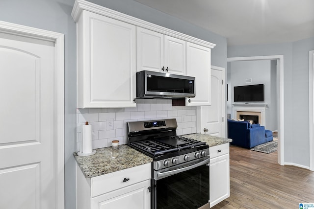 kitchen with appliances with stainless steel finishes, backsplash, white cabinetry, and light wood-style flooring