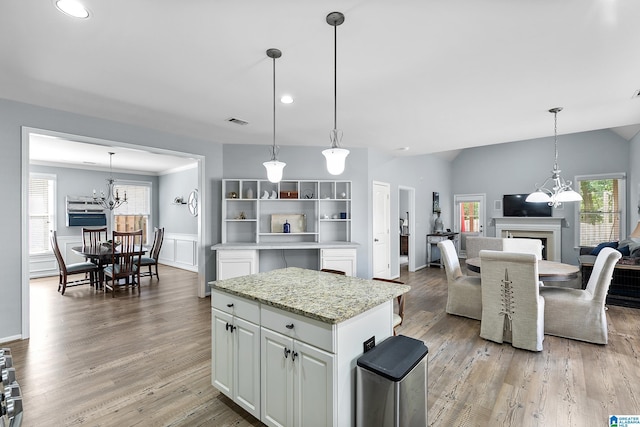 kitchen with a chandelier, white cabinetry, a fireplace, a kitchen island, and light wood finished floors