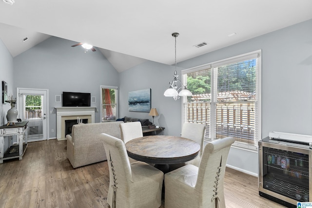 dining room with wine cooler, plenty of natural light, wood finished floors, a fireplace, and high vaulted ceiling