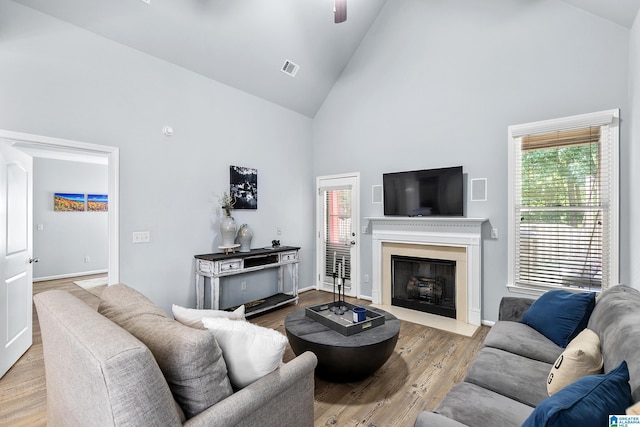 living room with high vaulted ceiling, plenty of natural light, a fireplace with flush hearth, wood finished floors, and baseboards