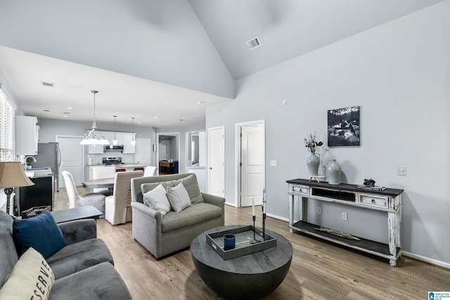living room with light wood finished floors, high vaulted ceiling, and baseboards