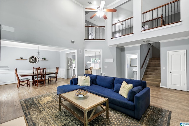 living room with a ceiling fan, stairway, wood finished floors, a high ceiling, and a chandelier