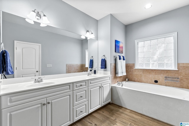 bathroom featuring wood finished floors, double vanity, and a garden tub