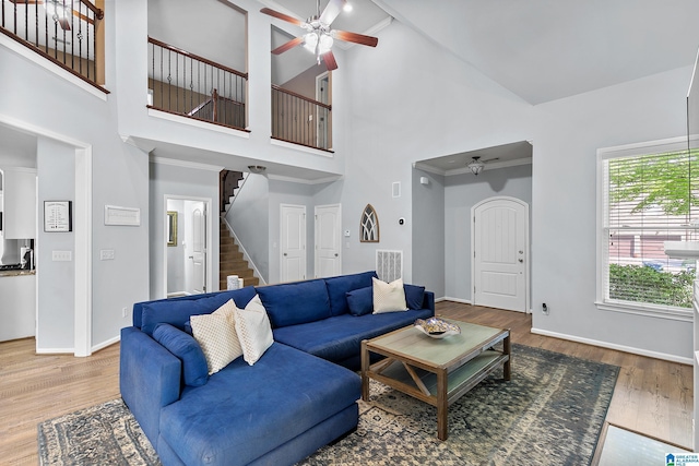 living area featuring a ceiling fan, stairs, high vaulted ceiling, wood finished floors, and baseboards