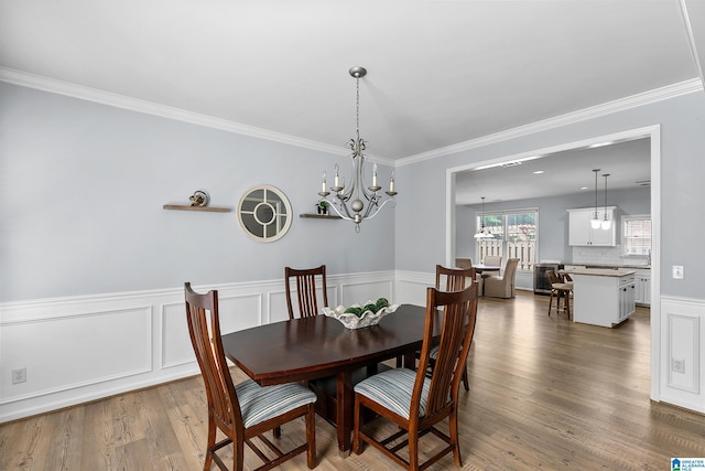dining room featuring ornamental molding, a chandelier, wood finished floors, a wainscoted wall, and a decorative wall