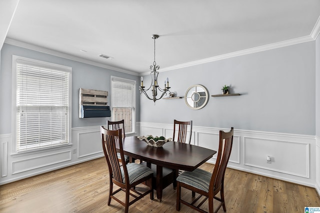 dining space with a chandelier, wainscoting, crown molding, wood finished floors, and a decorative wall