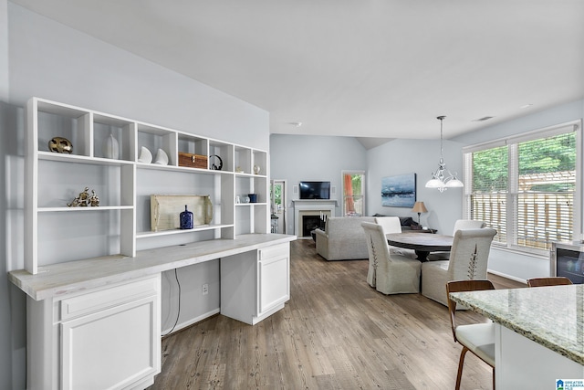 interior space featuring white cabinets, light stone counters, wood finished floors, pendant lighting, and a fireplace