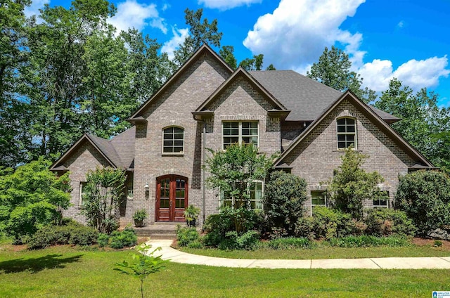 view of front of home with brick siding, a front yard, french doors, and a shingled roof