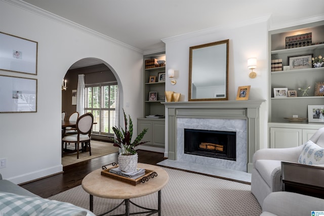 living room with wood finished floors, ornamental molding, arched walkways, a fireplace, and built in shelves