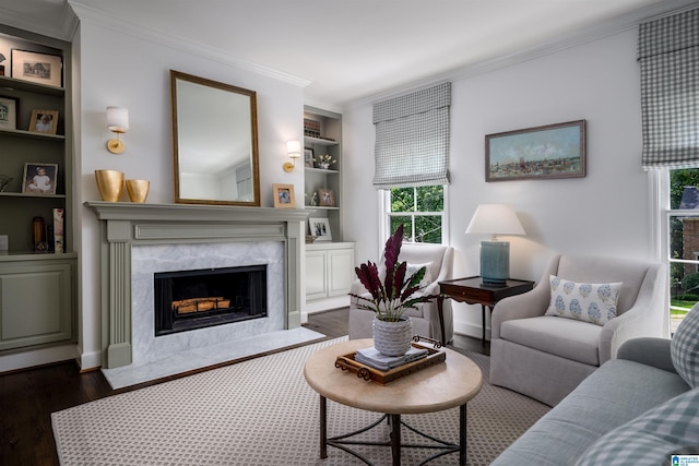 living room featuring dark wood finished floors, healthy amount of natural light, built in shelves, crown molding, and a fireplace