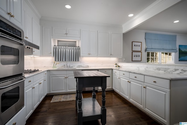 kitchen featuring stainless steel appliances, crown molding, decorative backsplash, white cabinets, and a sink