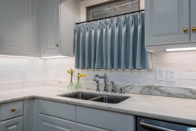 kitchen with a sink, dishwashing machine, tasteful backsplash, and light stone countertops