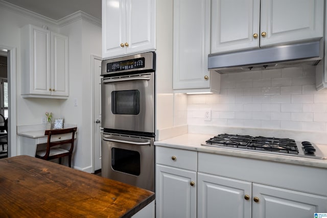 kitchen featuring appliances with stainless steel finishes, under cabinet range hood, decorative backsplash, white cabinets, and ornamental molding
