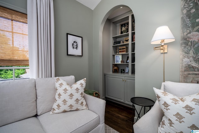 living area featuring dark wood-style flooring, arched walkways, and built in shelves