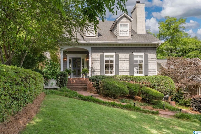 cape cod-style house featuring a chimney, a front yard, and a shingled roof