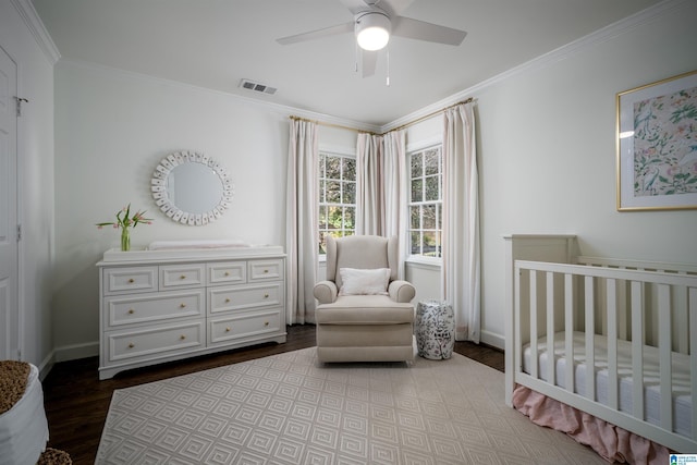bedroom with wood finished floors, crown molding, a crib, baseboards, and a ceiling fan