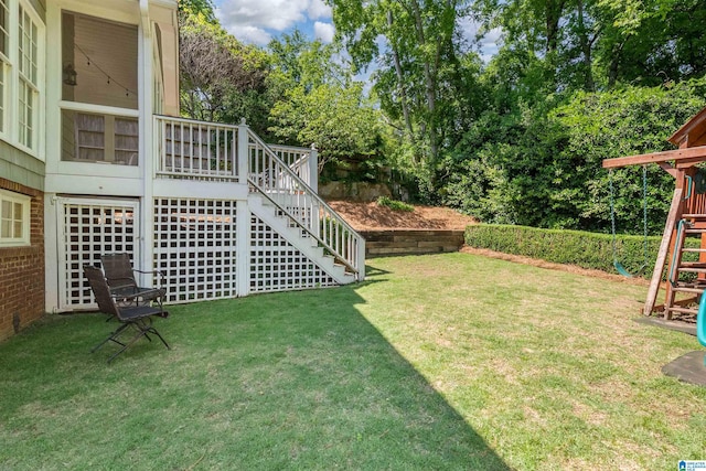 view of grassy yard with stairway, a playground, and view of wooded area
