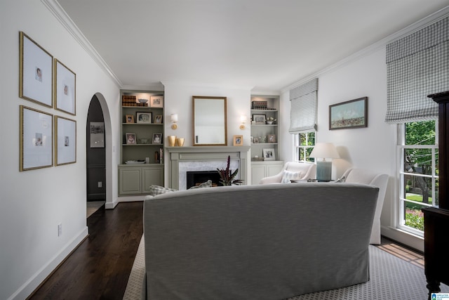 living room with ornamental molding, built in shelves, arched walkways, dark wood finished floors, and a premium fireplace