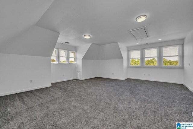 additional living space with attic access, dark colored carpet, vaulted ceiling, and baseboards