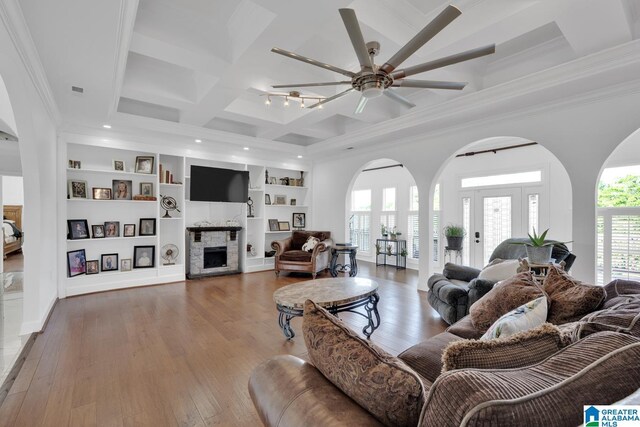 living room with a fireplace, a ceiling fan, wood finished floors, crown molding, and coffered ceiling