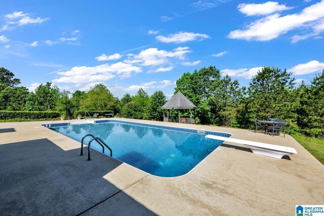 swimming pool featuring a gazebo, a patio, a diving board, and view of scattered trees
