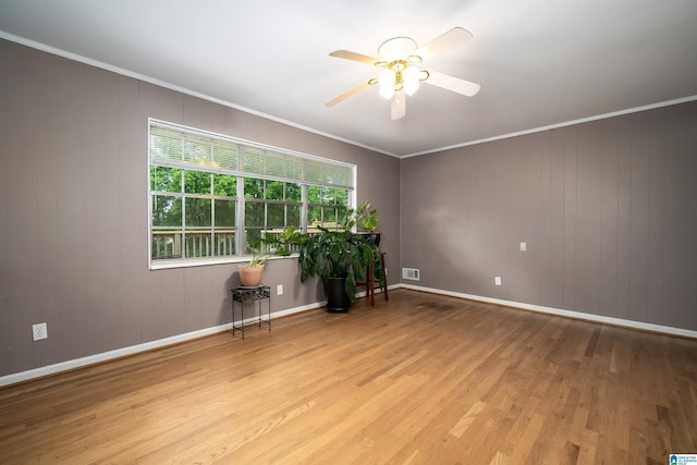 spare room featuring wood finished floors, a ceiling fan, ornamental molding, baseboards, and wood walls