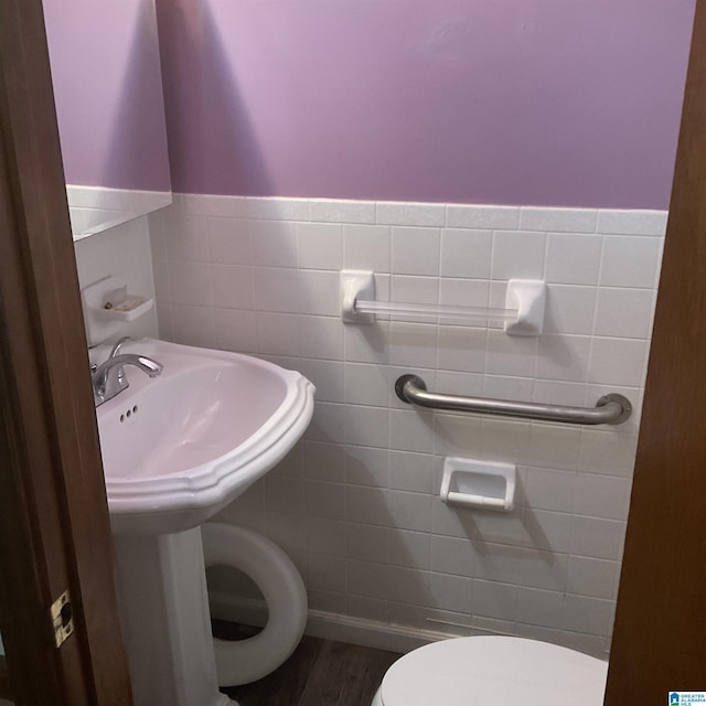 half bathroom featuring toilet, tile walls, wood finished floors, and a wainscoted wall