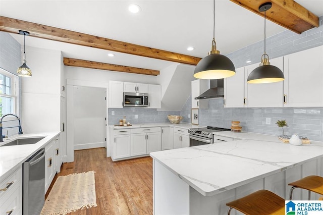 kitchen with a sink, appliances with stainless steel finishes, wall chimney exhaust hood, a peninsula, and light stone countertops