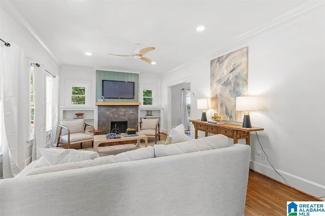 living area with crown molding, wood finished floors, baseboards, a fireplace, and a ceiling fan