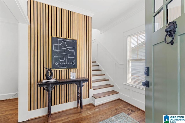 staircase featuring ornamental molding, wood finished floors, and a decorative wall
