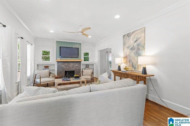 living area with crown molding, wood finished floors, baseboards, a fireplace, and a ceiling fan