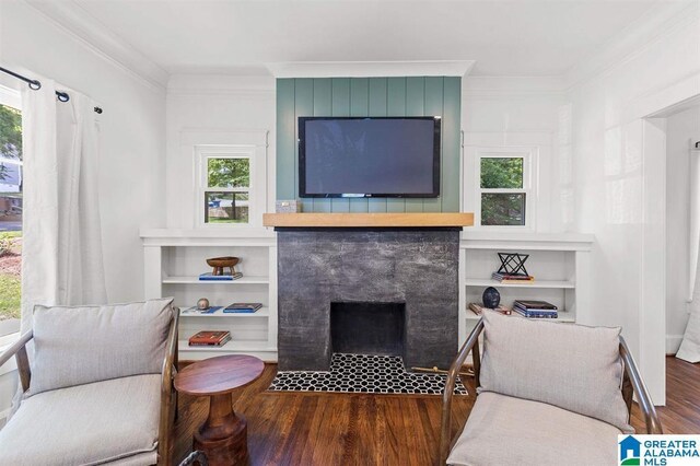living area featuring wood finished floors, a fireplace with flush hearth, ornamental molding, healthy amount of natural light, and built in shelves