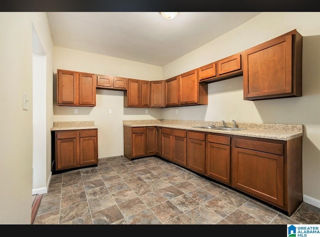 kitchen with brown cabinetry, baseboards, stone finish floors, light countertops, and a sink