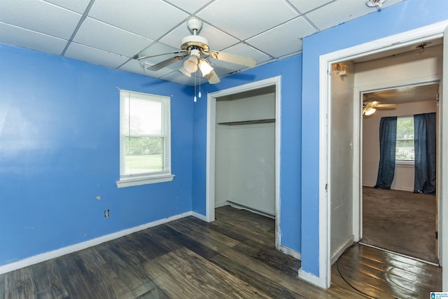unfurnished bedroom with a paneled ceiling, dark wood-type flooring, multiple windows, and a closet