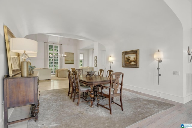 dining room featuring arched walkways, wood finished floors, a chandelier, and baseboards