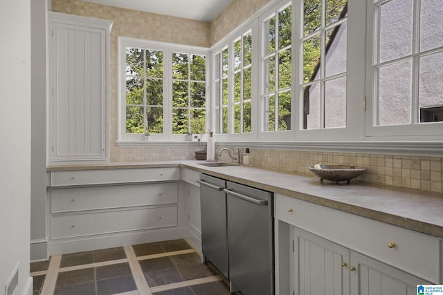 kitchen with decorative backsplash, a sink, light countertops, dishwasher, and dark stone finish flooring