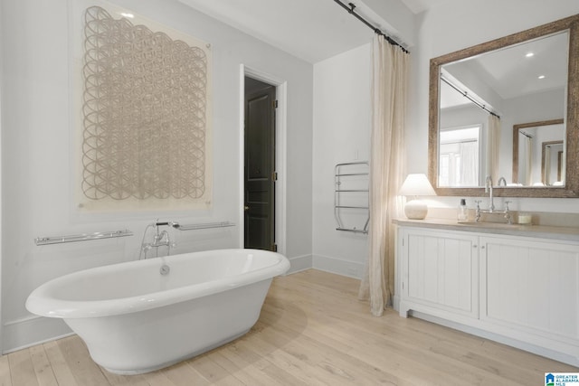 full bath featuring a soaking tub, wood finished floors, baseboards, and vanity