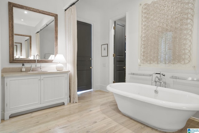 bathroom featuring a soaking tub, wood-type flooring, vanity, and baseboards