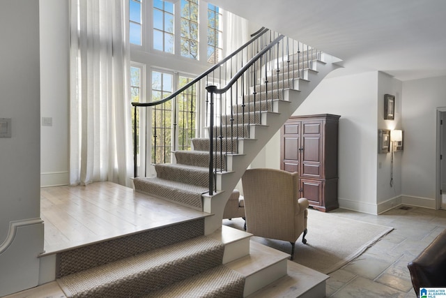 stairs with baseboards, stone tile floors, and a high ceiling