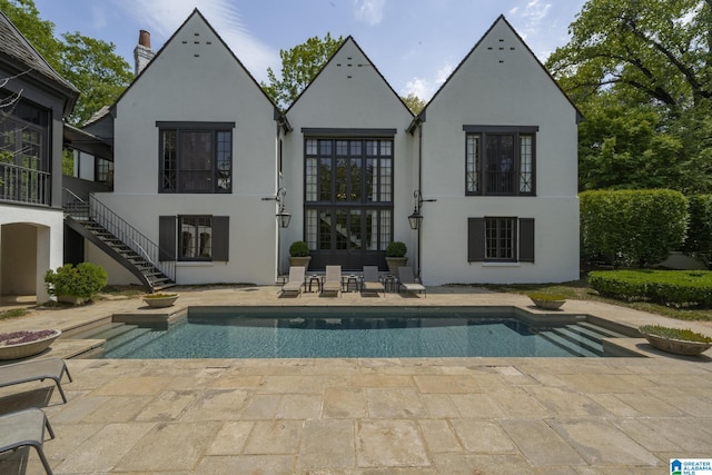 back of house with stucco siding, a patio, an outdoor pool, and stairs